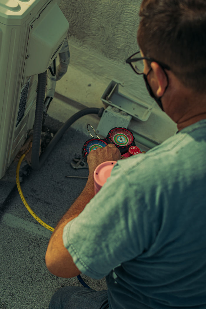 Technician servicing an air conditioning unit with tools and gauges