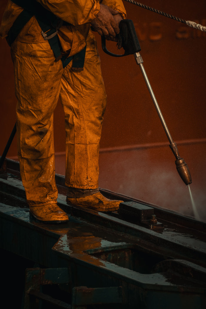 Worker in protective gear pressure-washing industrial equipment