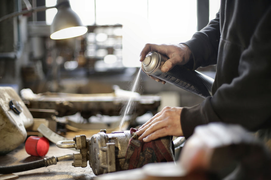 Worker cleaning a machine part with a spray can in a workshop